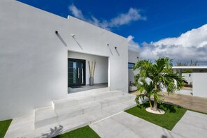 Een modern gebouw met een witte gevel, een glazen entree en een kleine tuin met een palmboom.