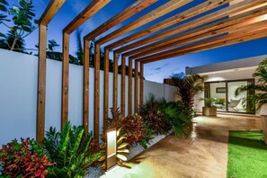 Eine moderne Außenpatio mit Holz-Pergolen, verschiedenen Pflanzen und einer Glastür zu einem Innenraum.