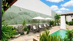 A poolside area with lounge chairs and umbrellas, a stone wall, and a large green wall with palm leaf patterns. - 5-bedroom bed & breakfast in welcoming Mérida with AC (Mérida)