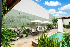 A poolside area with lounge chairs and umbrellas, a stone wall, and a large green wall with palm leaf patterns. - 5-bedroom bed & breakfast in welcoming Mérida with AC (Mérida)