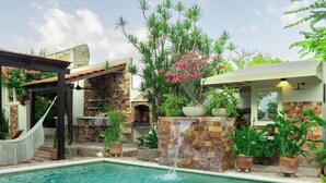A pool with a waterfall feature, surrounded by potted plants and a stone wall. - 5-bedroom bed & breakfast in welcoming Mérida with AC (Mérida)