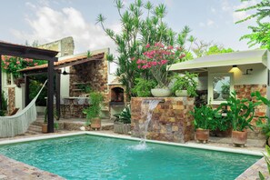 A pool with a waterfall feature, surrounded by potted plants and a stone wall. - 5-bedroom bed & breakfast in welcoming Mérida with AC (Mérida)