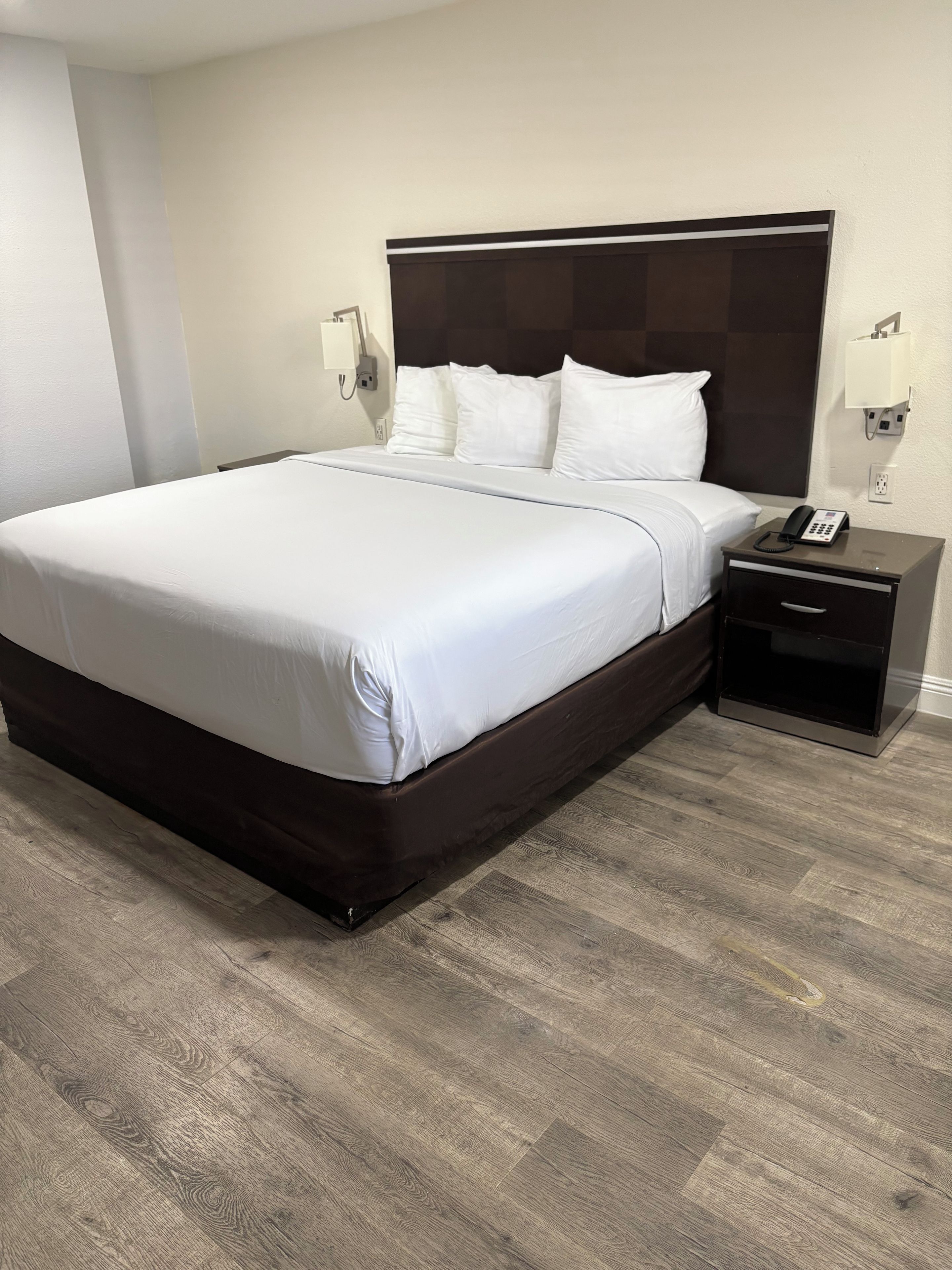 A hotel room with a large bed, a bedside table with a phone, and a wall-mounted light.