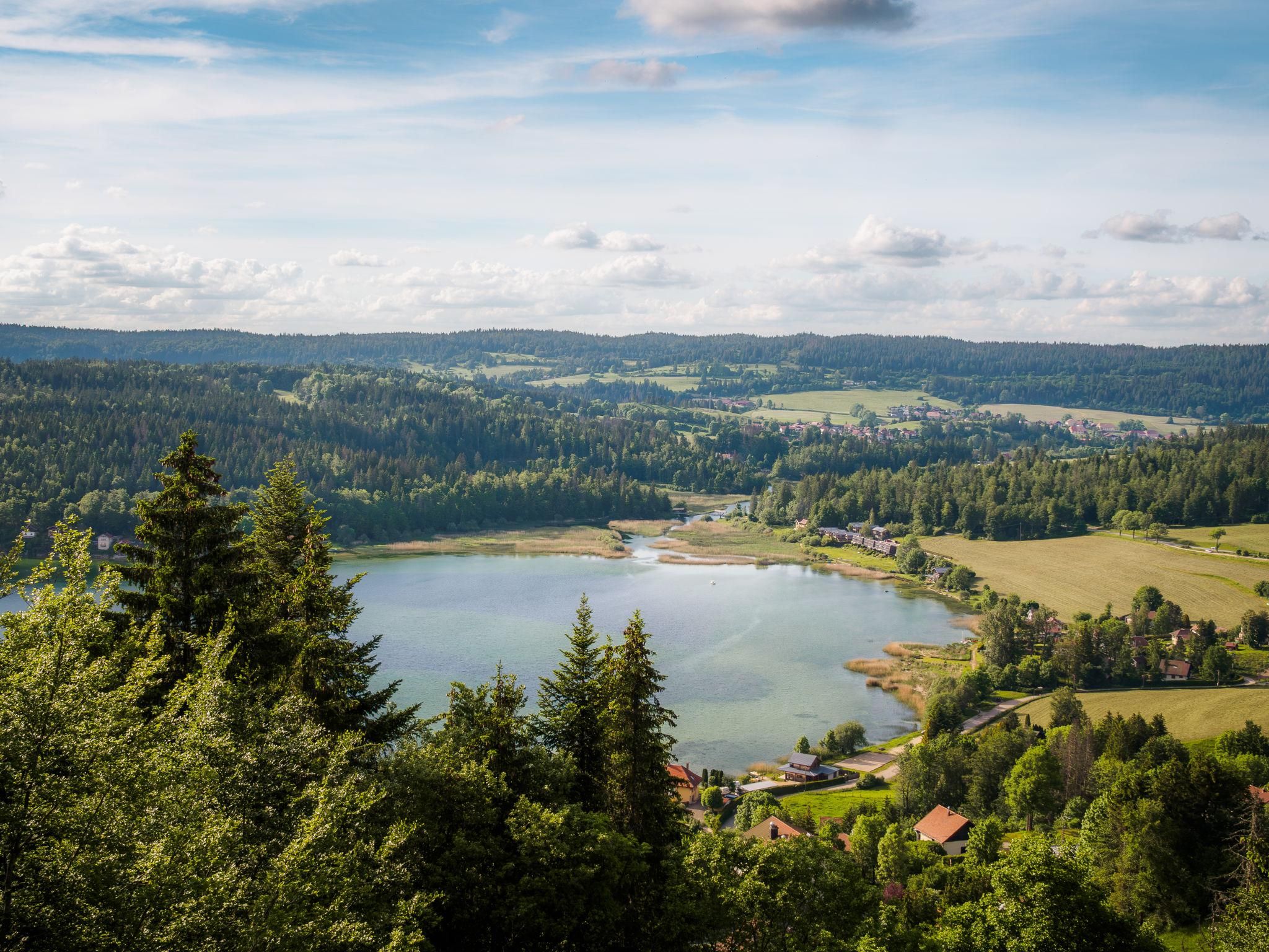 Ein See, umgeben von bewaldeten Hügeln und einer kleinen Siedlung mit Häusern.
