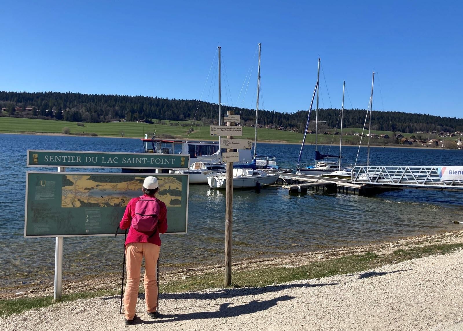 Eine Person steht bei einem Schild mit einer Karte in der Nähe eines Hafens mit vertankten Booten.