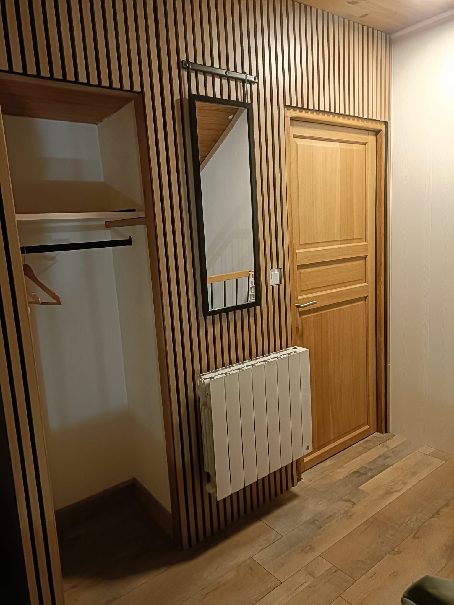 Huone, jossa on puinen vaatekaappi, peili ja patteri.