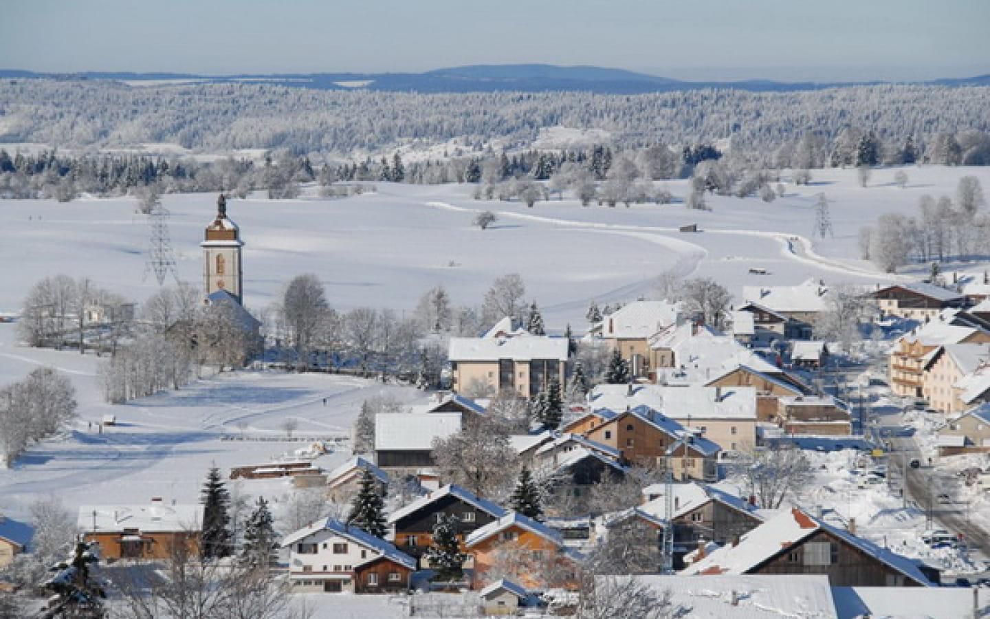 Un pueblo cubierto de nieve con edificios tradicionales, una imponente torre de iglesia y una vista despejada del paisaje nevado circundante.