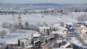 Un pueblo cubierto de nieve con edificios tradicionales, una imponente torre de iglesia y una vista despejada del paisaje nevado circundante.