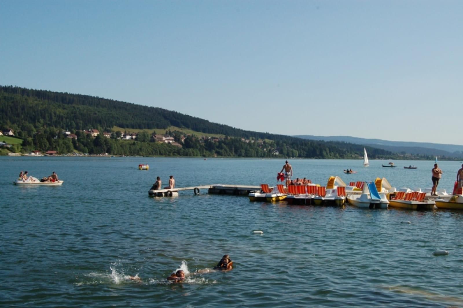 Un lac avec des bateaux, un quai et des gens qui se baignent.
