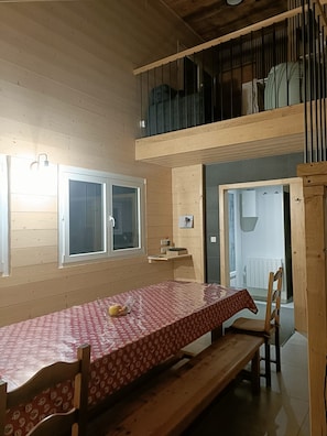 A dining area with a table and benches, a window, and a door leading to another room.