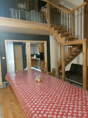 A room with a dining table, a sofa, a staircase, and a kitchen area.