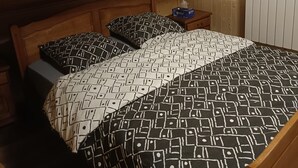Quarto pequeno com cama de solteiro, teto inclinado, paredes de madeira e radiador.