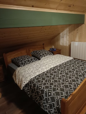 A small, single-bed room with a sloped ceiling, wooden walls, and a radiator.