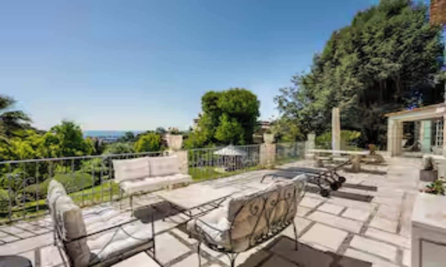 An outdoor patio with a sofa and chairs, a stone table, and a view of the surrounding greenery and landscape.