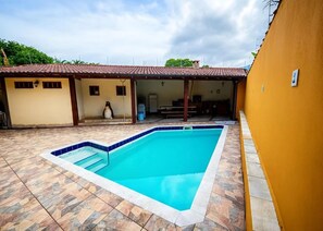 A swimming pool with a tiled deck, a covered patio area, and a building with a tiled roof. - House with 4 suites, 100m from the beach | Pool & Gourmet Kitchen | 1.2km from the village (Ilhabela)
