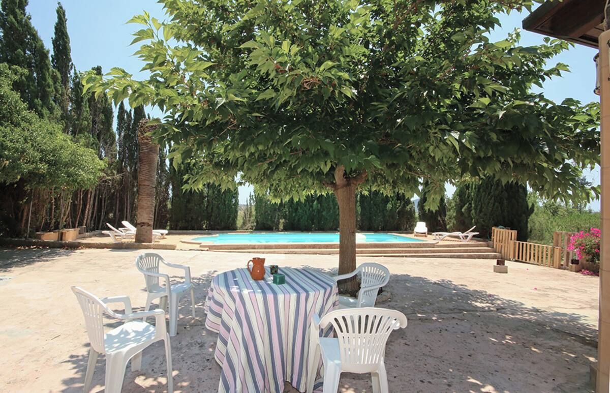 A poolside area with a table and chairs, surrounded by trees and a clear view of the pool.