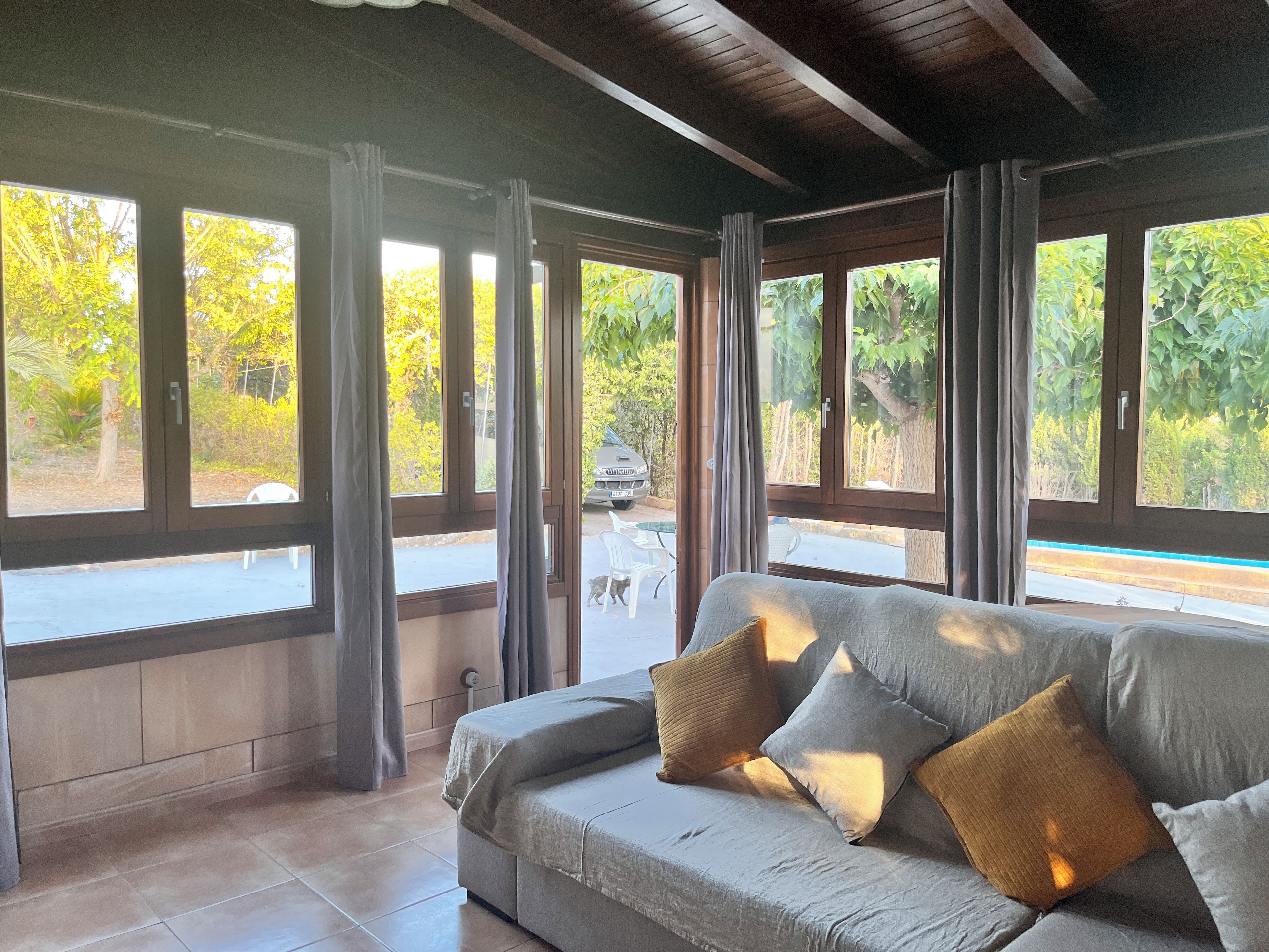 Una habitación con sofá, cortinas y ventanas amplias con vistas a un jardín.