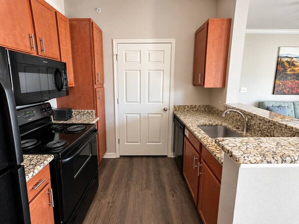 A kitchen with wooden cabinets, a black stove, a microwave, and a granite countertop.