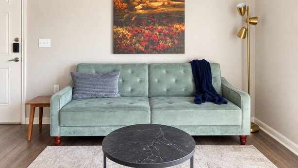 Ein Wohnzimmer mit einem grünen Sofa, einem runden schwarzen Couchtisch und einem Landschaftsbild.