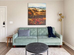 A living room with a green sofa, a round black coffee table, and a painting of a landscape.