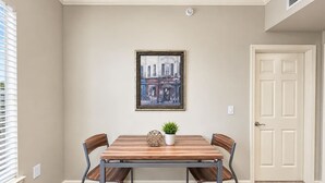 Un coin repas avec une table en bois et quatre chaises, un tableau encadré au mur et une porte sur la droite.