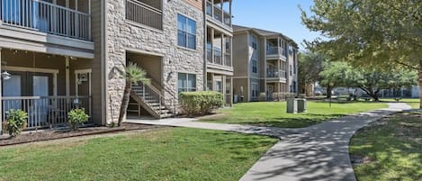 A multi-story residential building with balconies, a stone facade, and a well-maintained lawn.