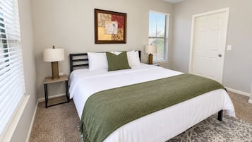A bedroom with a bed, two bedside tables, a lamp on each table, a door, and a window with blinds.