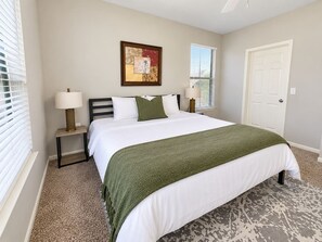 A bedroom with a bed, two bedside tables, a lamp on each table, a door, and a window with blinds.