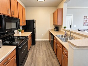 A modern kitchen with wooden cabinets, a black refrigerator, a microwave, a stove, and a sink. - Sleepover | Breezy 1BD/1BA + Gym - Corpus Christi (Corpus Christi)