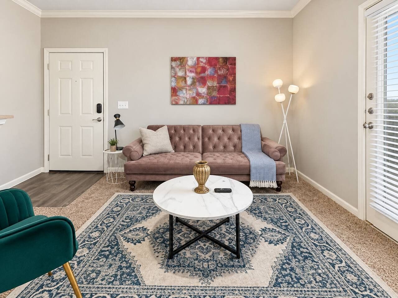 A living room with a tufted sofa, a round coffee table, a patterned rug, and a door with a light switch.