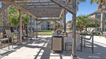 An outdoor patio with a pergola, seating, and a grill area.
