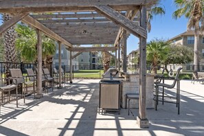 An outdoor patio with a pergola, seating, and a grill area.