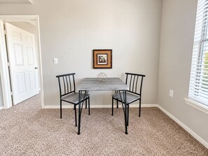 A room with a table and chairs, a framed picture on the wall, and a window with blinds. - Sleepover | Bright 1BD/1BA + Gym - Corpus Christi (Corpus Christi)
