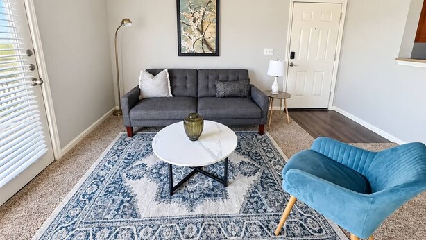 En stue med sofa, sofabord, blå stol, gulvlampe og en dør.