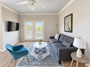 A living room with a sofa, a blue chair, a coffee table, a lamp, and a TV.
