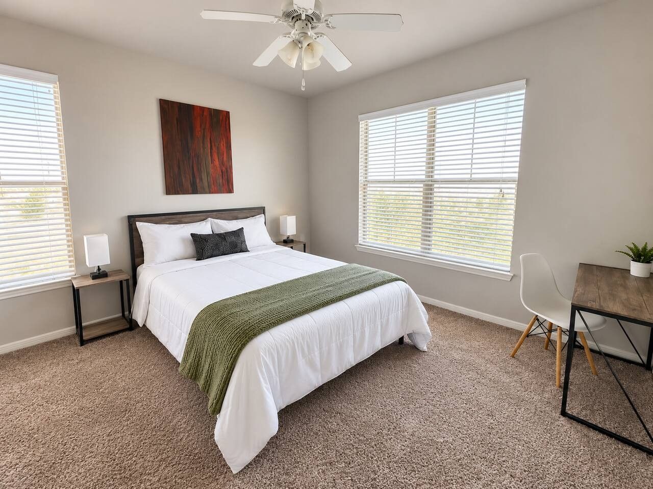 A bedroom with a bed, bedside tables, a desk, a chair, and a ceiling fan.