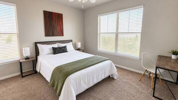 A bedroom with a bed, bedside tables, a desk, a chair, and a ceiling fan.