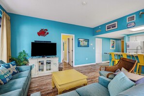 A living room with a television, sofa, and yellow coffee table. - Beach Colony 210 - Steps to the Beach (Myrtle Beach)
