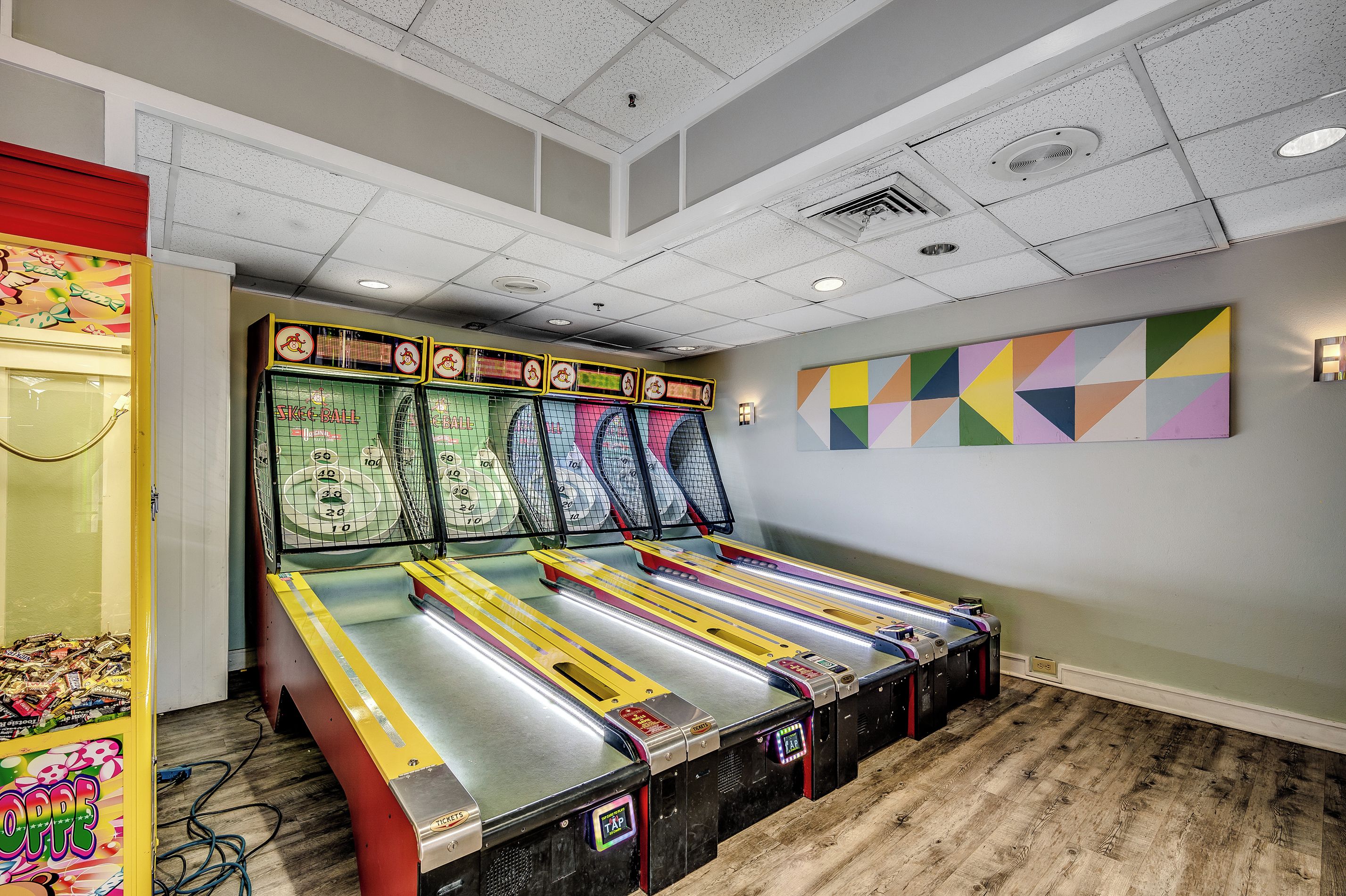 A room with four pinball machines, a colorful abstract painting, and a wooden floor.