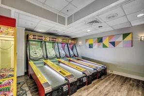 Um quarto com quatro máquinas de pinball, uma pintura abstrata colorida e piso de madeira.