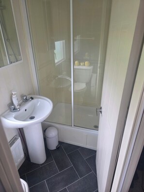 A bathroom with a white sink, a glass shower enclosure, and a toilet visible through the glass. - 2-bed - Sleeps 6 - Free Parking (Arbroath)