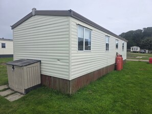 A single-story mobile home with a flat roof, a small attached garage, and a grassy yard.