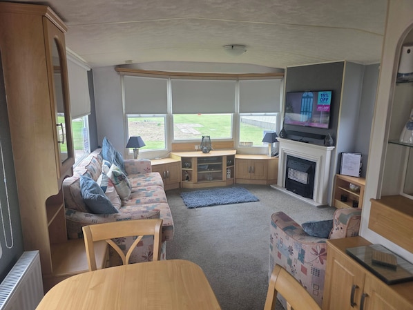 A compact living space with a sofa, a table, a fireplace, and a television. - 2-bed - Sleeps 6 - Free Parking (Arbroath)