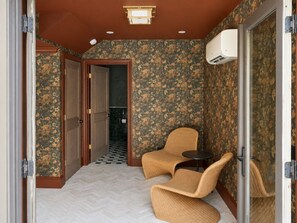A hallway with a checkered floor, a wicker chair, a small table, and a door leading to a bathroom. - Maplewood Estate • Heated Pool, Hot Tub, Gym, Grill, Fire Pit (Nashville)