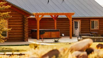 Una cabaña de troncos con porche cubierto, mobiliario exterior y jacuzzi.