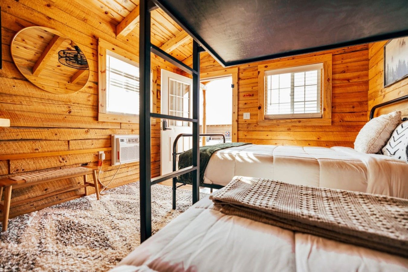 A cozy wooden cabin room with a bed, a bench, and a window.