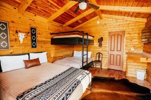 A cabin with a bunk bed, a single bed, a wooden ceiling, a ceiling fan, a door, and a small chair.