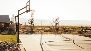 Una cancha de baloncesto al aire libre con un aro, una estructura de juegos de madera y una casa al fondo.