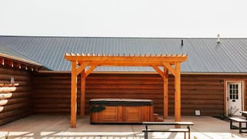 Een overdekt buitengebied met een houten pergola, een jacuzzi en picknicktafels.