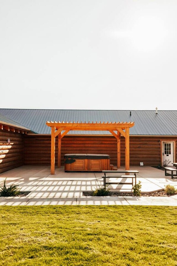 A covered outdoor area with a wooden pergola, a hot tub, and picnic tables.